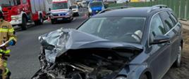 Na zdjęciu znajduje się wrak pojazdu stojącego na drodze w tle widać strażaka, wozy strażackie, ZRM i policja