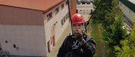 przy pomocy sprzętu zjazdowego, strażak opuszcza się na linie ze wspinalni. Funkcjonariusz jest odpowiednio zabezpieczony linką asekuracyjną oraz ma niezbędne elementy ochraniające głowę i dłonie. 