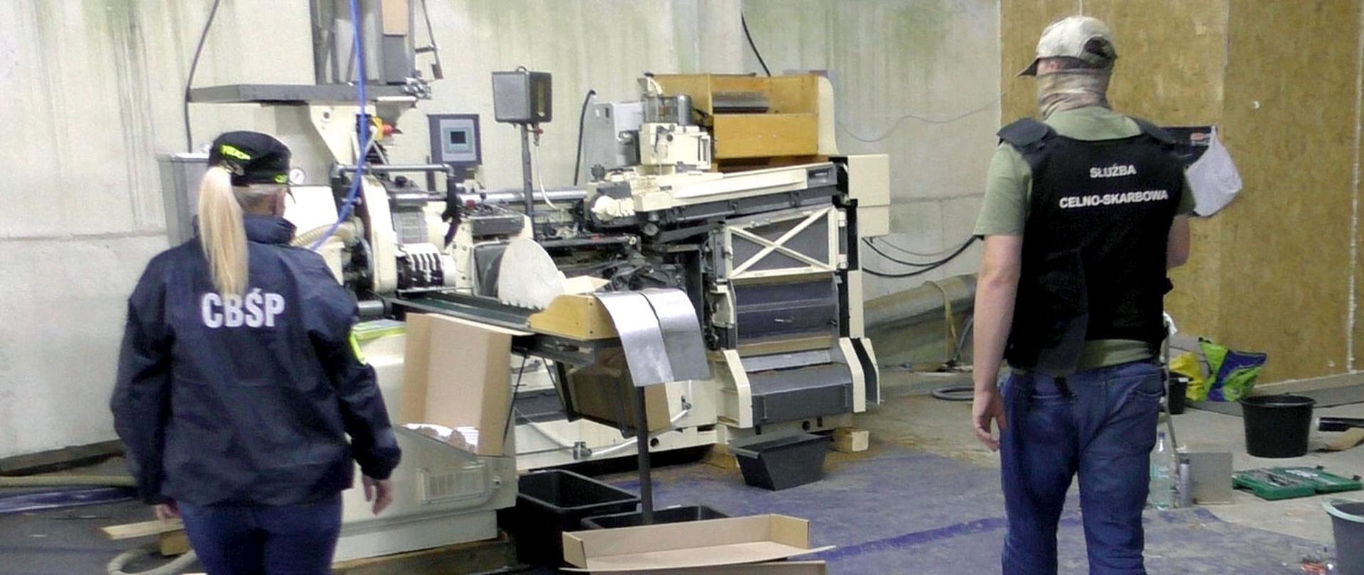 Funkcjonariuszka CBŚP i funkcjonariusz Służby Celno-Skarbowej KAS w wykrytej fabryce nielegalnych papierosów.