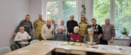 Grupa seniorów wraz ze strażakami pozuje do zdjęcia za stołem 