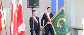 Trzech uczniów ubranych na galowo wprowadza sztandar szkoły.