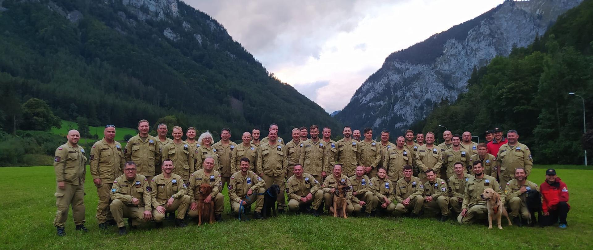 Grupowe zdjęcie polskich strażaków wraz z psami ratowniczymi, w tle góry