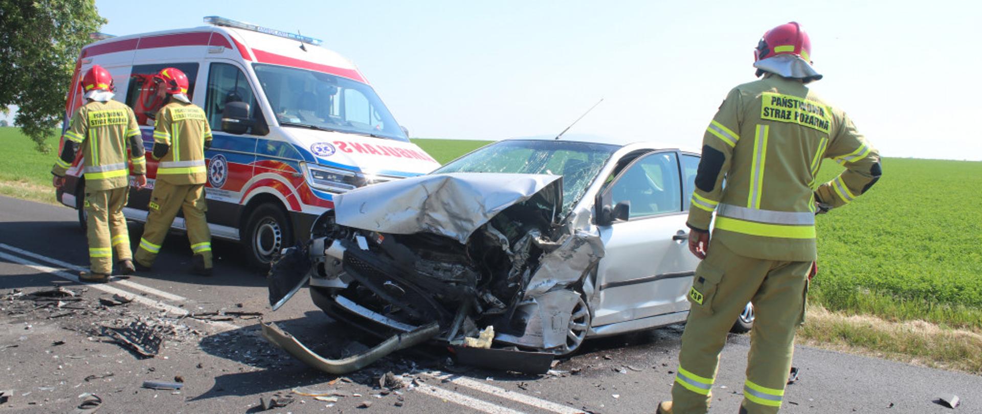 Na zdjęciu znajduje się uszkodzony samochód osobowy, karetka pogotowia oraz strażacy.
