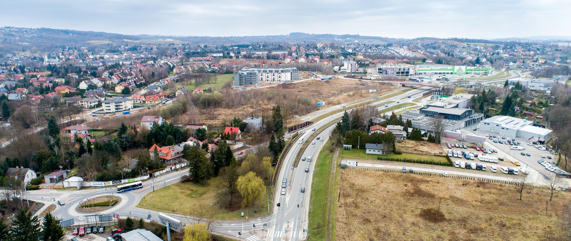 Widok z góry na zjazd z Ronda Wieliczan w kierunku DK94 ("starej czwórki"). Widoczna sygnalizacja świetlna przy ulicy Krakowskiej. Wokół liczne zabudowania i sklepy wielkopowierzchniowe. 