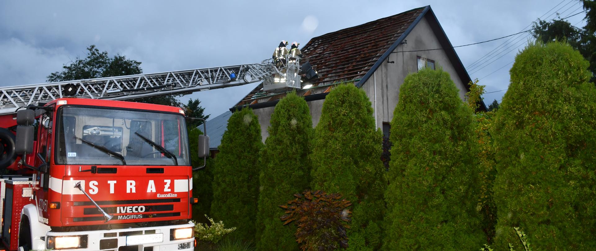 Na zdjęciu widzimy strażaków pracujących na podnośniku, którzy zabezpieczają dach budynku.