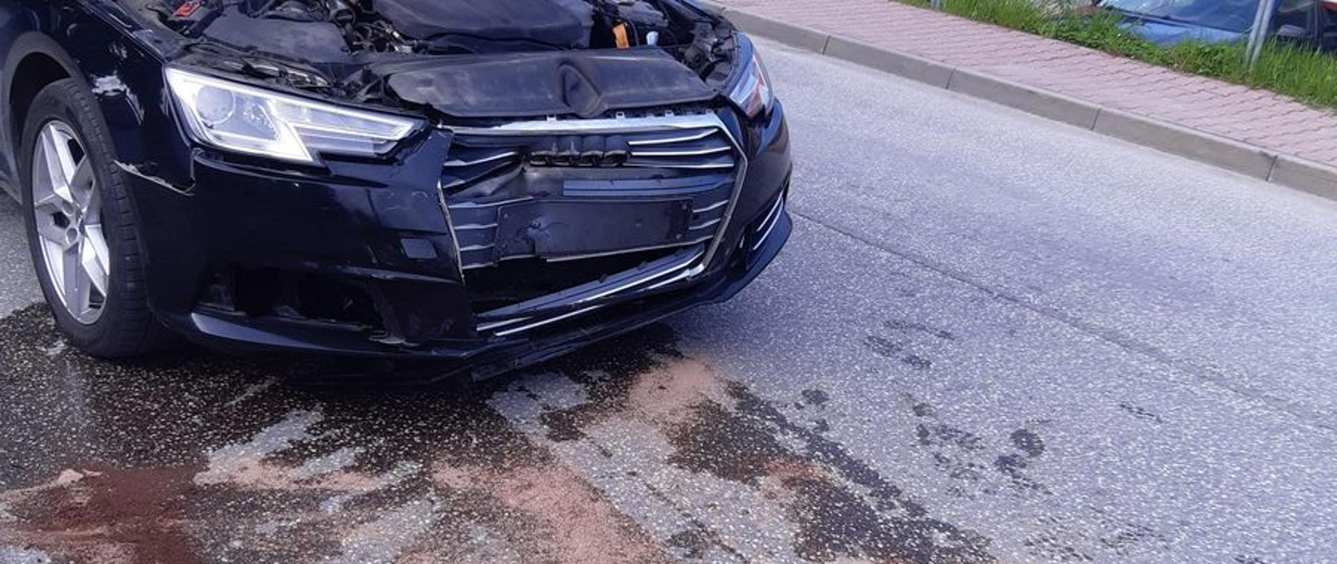 Uszkodzony samochód z podniesioną klapą silnika. Przed samochodem na jezdni rozlana substancja zasypana sorbentem.