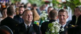 Na zajęciu widoczni dwaj strażacy w mundurach wyjściowych uczestniczący w Gali Honorowych Dawców Krwiodawców powiatu gorlickiego siedzący przy stoliku w oddali zaroszeni krwiodawcy.