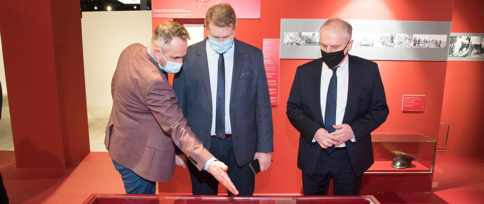 wizyta ministra w muzeum II WŚ ogląda wraz z przewodnikiem fragmenty odzieży