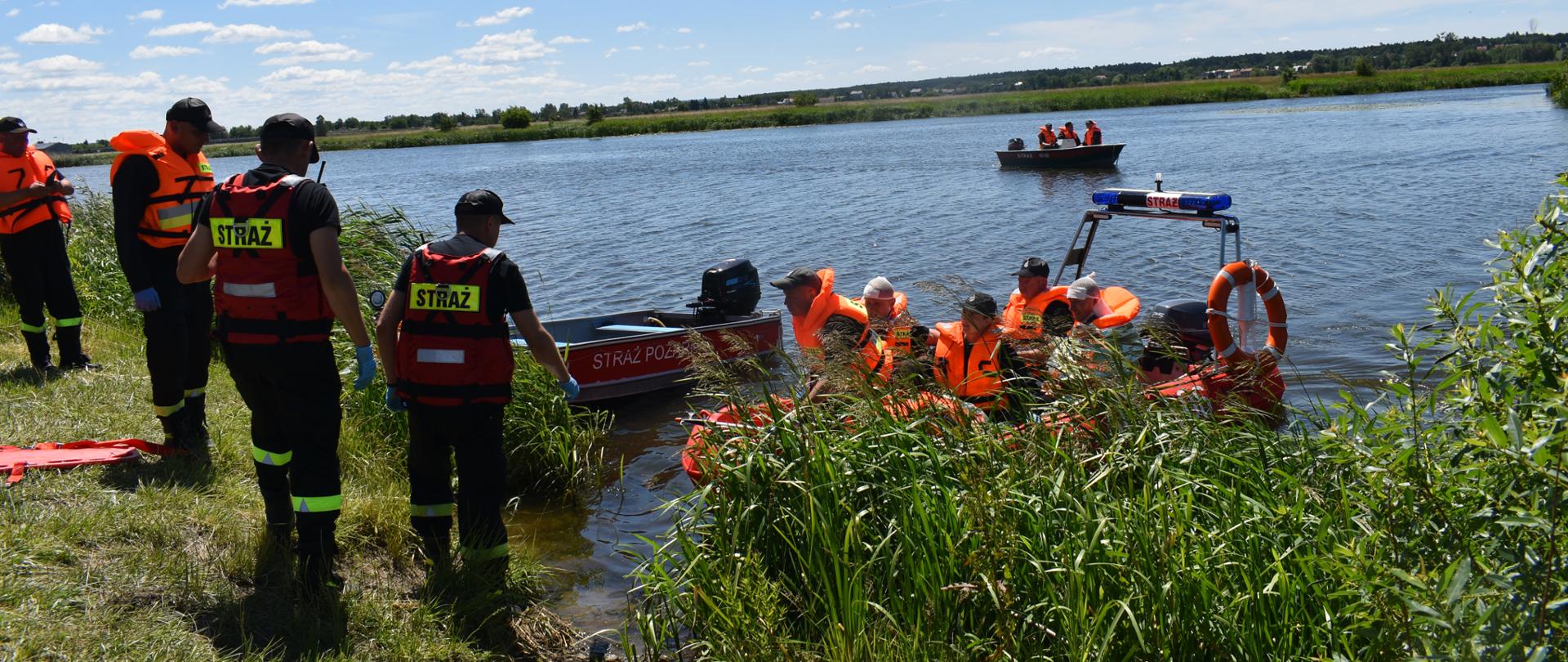 Strażacy ewakuują harcerzy z wyspy przy użyciu pontonów i łodzi. 
