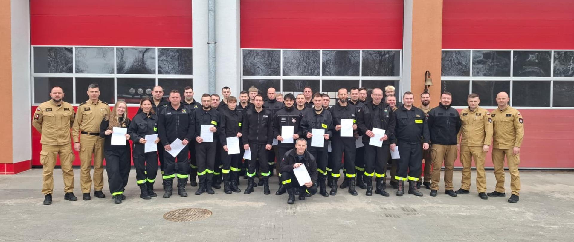 Strażacy z certyfikatami stoją przed komendą.