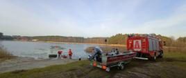 Na zdjęciu samochód strażacki z podczepiona łódką w tle strażacy