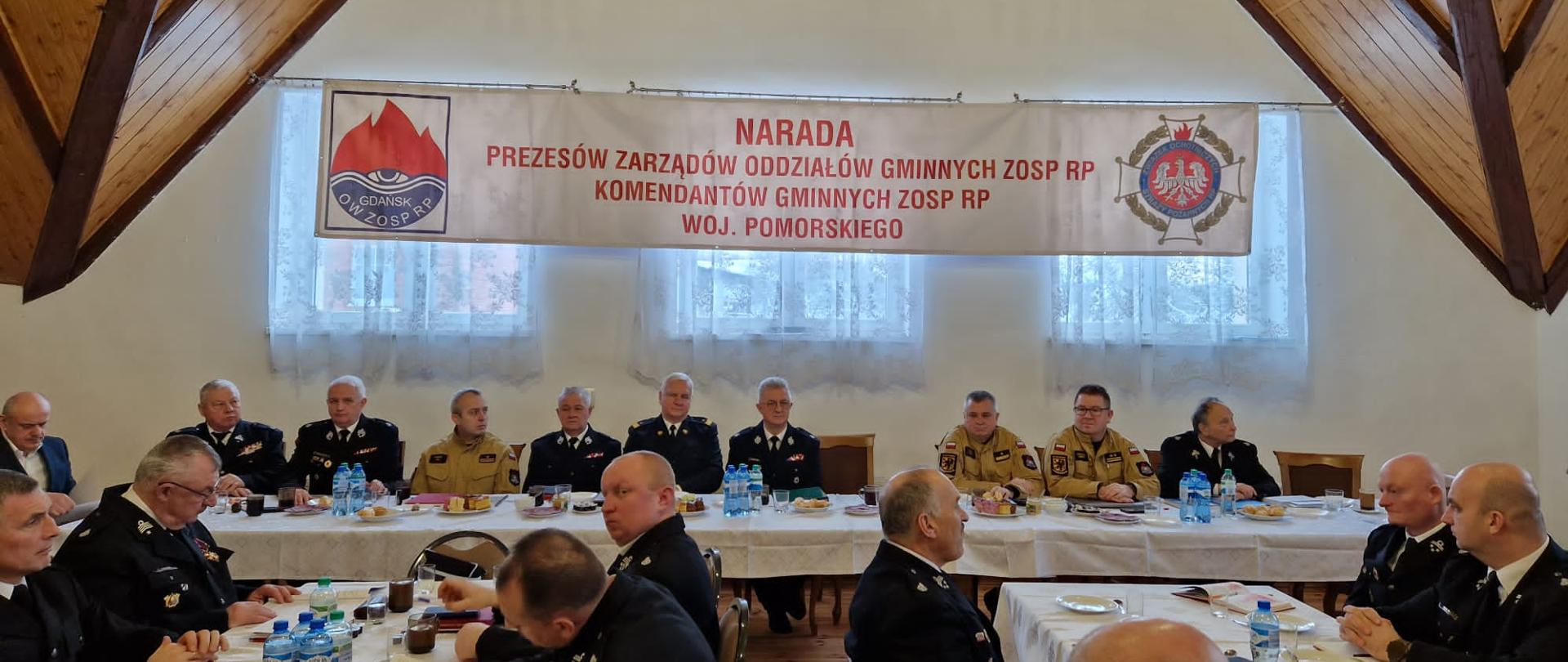 Strażacy ochotniczych straży pożarnych oraz Państwowej Straży Pożarnej siedzą za stołami.