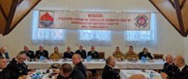 Strażacy ochotniczych straży pożarnych oraz Państwowej Straży Pożarnej siedzą za stołami.