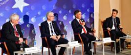 Wiceminister Zbigniew Gryglas przemawia do mikrofonu. Obok siedzą pozostali paneliści. W tle ścianka z logo Forum Ekonomicznego.