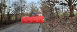Zdjęcie przedstawia miejsce wypadku drogowego zastawione parawanem i stojący samochód pożarniczy z włączonymi sygnałami świetlnymi