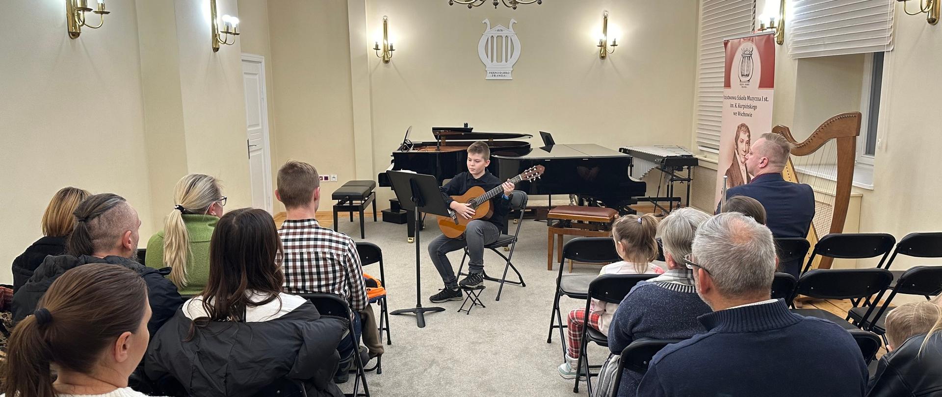 Występ ucznia klasy gitary podczas koncertu w auli szkoły. 