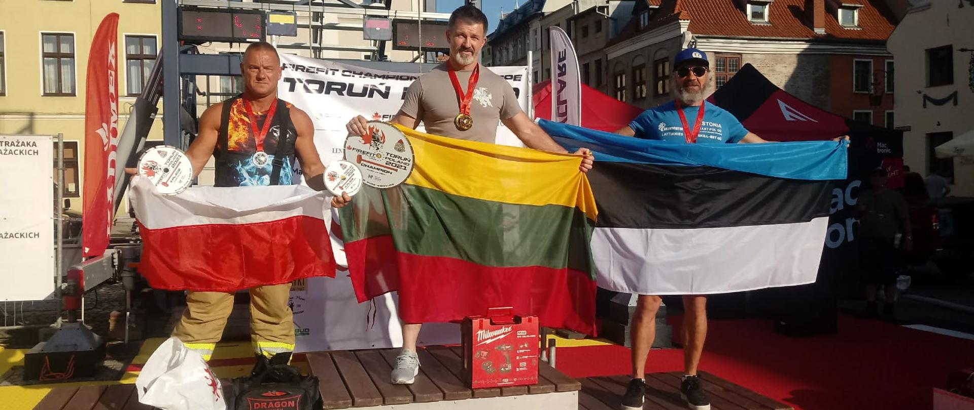 Zdjęcie przedstawia zawodników stojących na podium z flagami swoich państw w zawodach firefit Toruń.