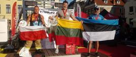 Zdjęcie przedstawia zawodników stojących na podium z flagami swoich państw w zawodach firefit Toruń.