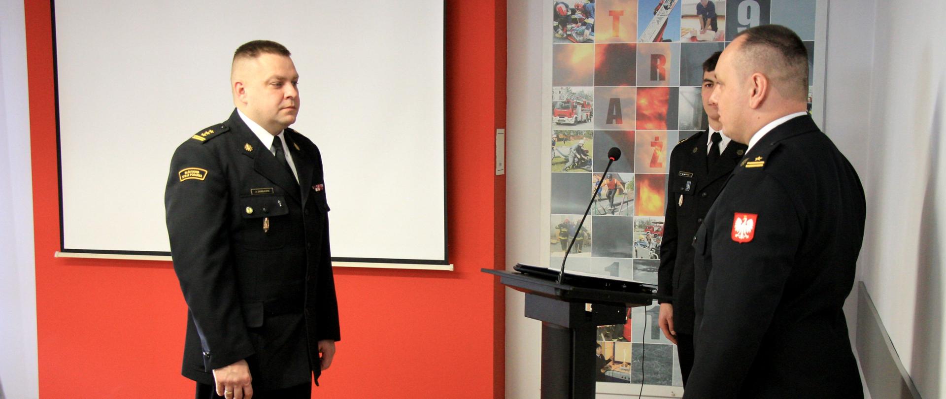 składanie meldunku strażaka drugiemu strażakowi, w tle duży biały ekran do projektora