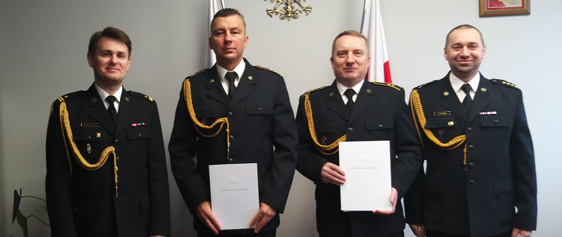 starszy aspirant Leszek Bąk oraz starszy aspirant Mariusz Zakrzewski trzymają decyzje zwalniające ze służby w Państwowej Straży Pożarnej w towarzystwie Zastępcy Komendanta Powiatowego Państwowej Straży Pożarnej oraz Dowódcy Jednostki Ratowniczo Gaśniczej w Goleniowie