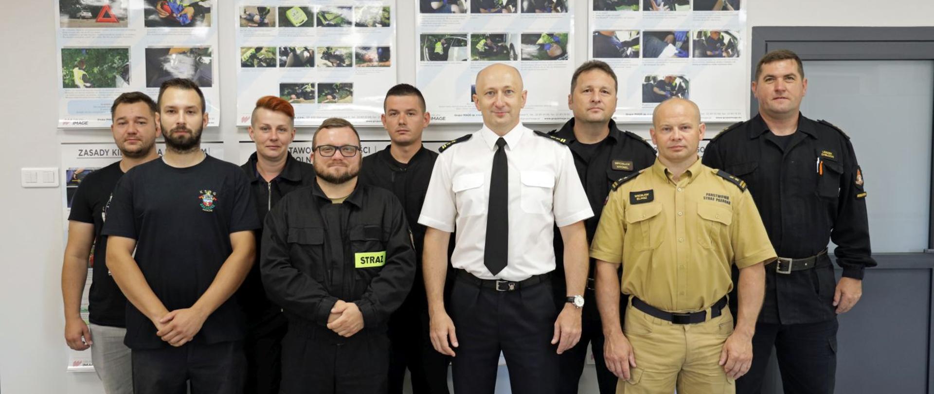 Wspólne pamiątkowe zdjęcie na tle tablic szkoleniowych w sali dydaktycznej Ośrodka Szkolenia KW PSP w Opolu. Na zdjęciu uczestniczy szkolenia przygotowującego do egzaminu na prawo jazdy kategorii C, instruktorzy, Naczelnik Ośrodka Szkolenia KW PSP w Opolu oraz p.o. Zastępca Opolskiego Komendanta Wojewódzkiego PSP w Opolu bryg. Dariusz Gieroń.