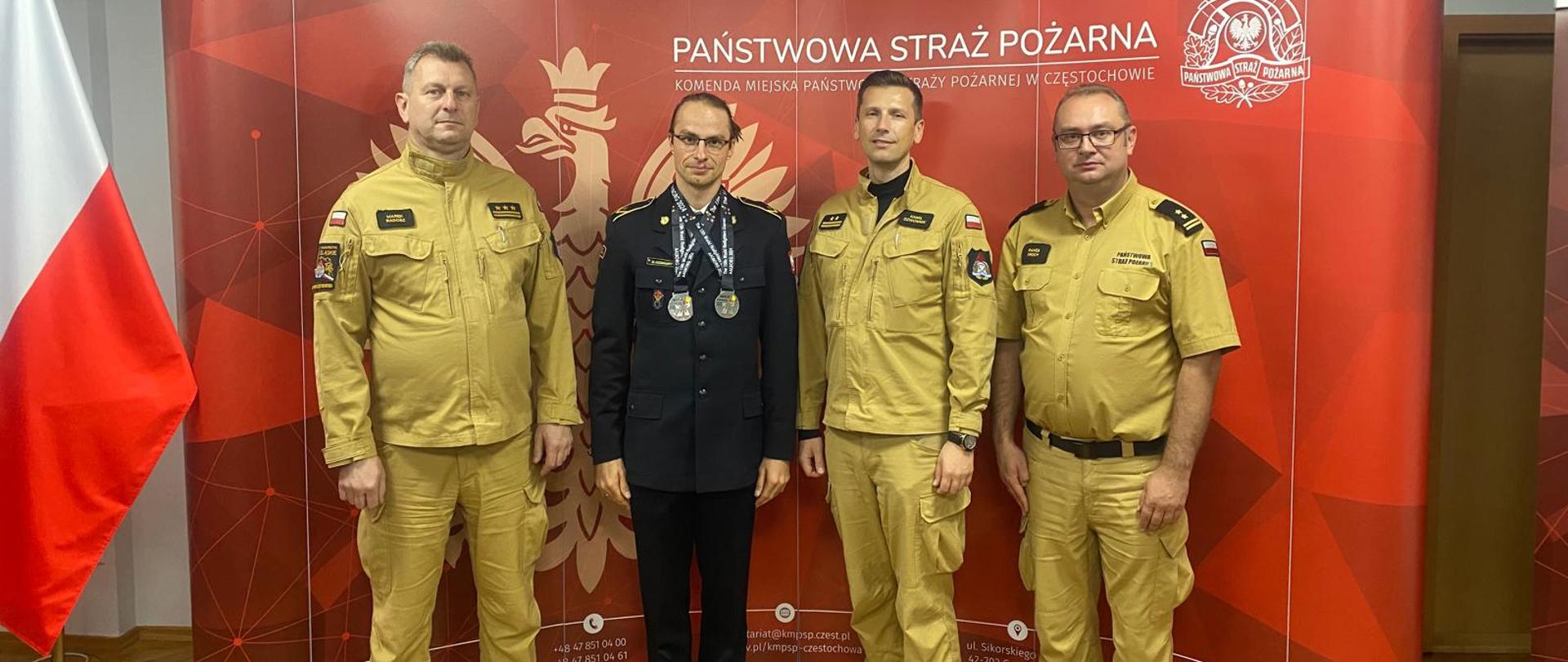 Na zdjęciu ustawianych czterech funkcjonariuszy Państwowej Straży Pożarnej jeden z nich na szyi ma zawieszone dwa medale