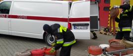 Strażacy wypakowują węże strażackie z busa Komendy Powiatowej PSP w Żyrardowie.