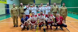 Strażacy, zawodnicy drużyny, która zajęła 2 miejsce pozują do zdjęcia razem z komendantami na boisku hali sportowej.