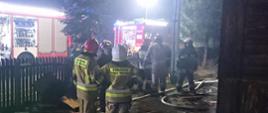 Strażacy oraz samochody gaśnicze przed spalonym budynkiem mieszkalnym 