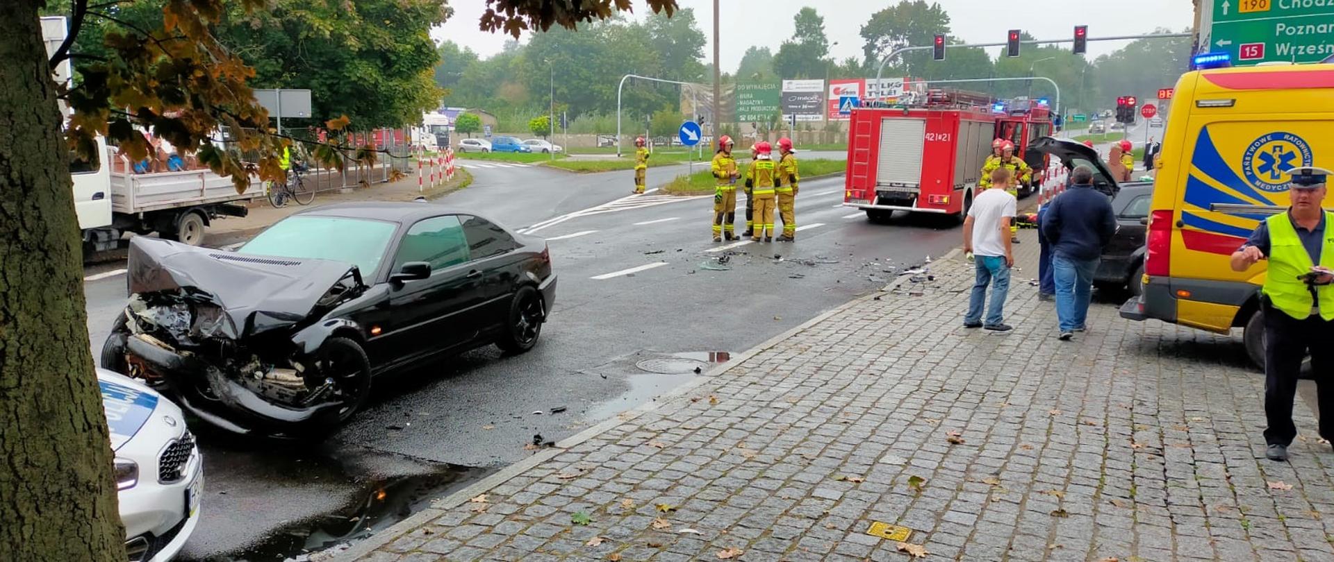 Na zdjęciu widać miejsce wypadku, okolice krzyżówki ze światłami świetlnymi. Po prawej stronie zdjęcia widać karetkę a przy nim policjanta. Dalej w części środkowej widać wóz strażacki oraz stojących strażaków. Po lewej stronie zdjęcia widać przód rozbitego pojazdu oraz kawałek radiowozu