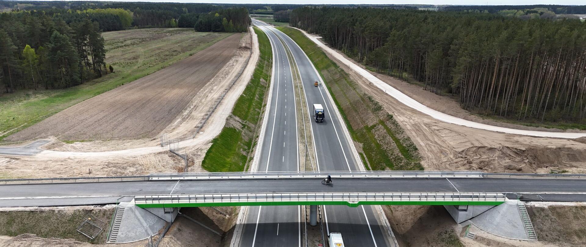 Dwujezdniowa droga ekspresowa widziana z lotu ptaka. Trwają ostatnie prace m.in. przy oznakowaniu poziomym malowana jest linia ciągła miedzy pasem ruchu a pasem awaryjnym. Na pierwszym planie poprzeczny wiadukt nad dwiema jezdniami eski