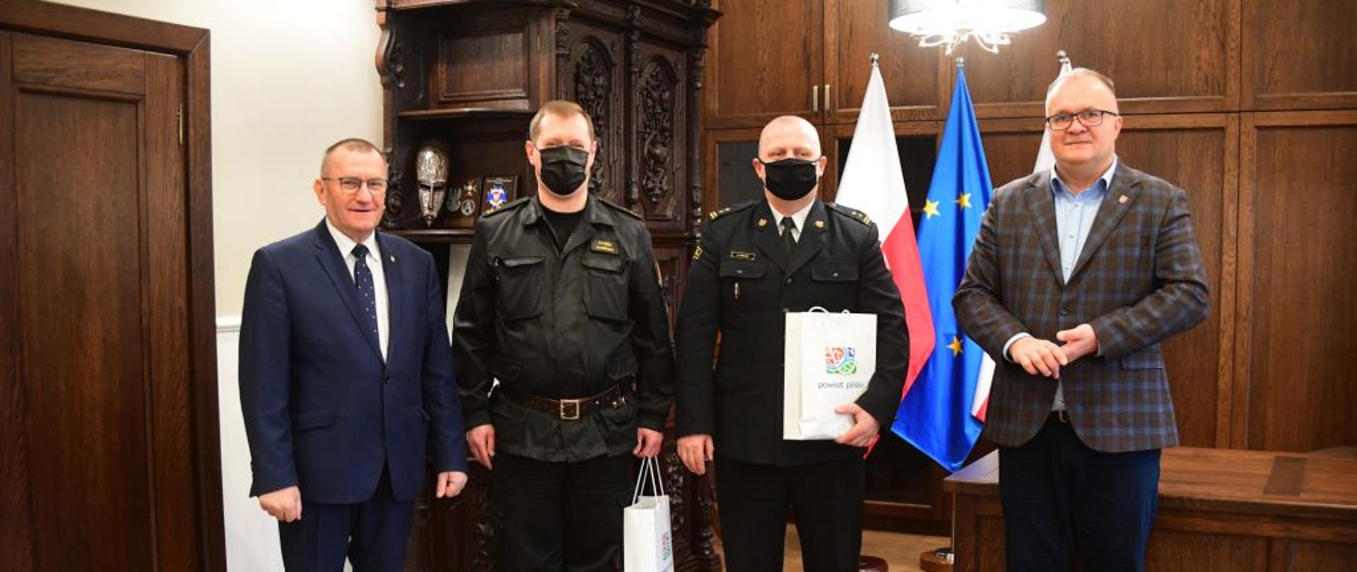 Na zdjęciu widnieje spotkanie pełniącego obowiązki komendanta Powiatowego PSP w Pile ze Starostą Pilskim. Spotkanie odbyło się wewnątrz oświetlonego pomieszczenia. 