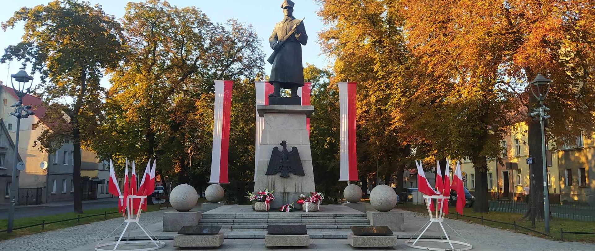 84. rocznica agresji ZSRR na Polskę.Zdjęcie przedstawia Pomnik Żołnierza Polskiego w Rawiczu. Żołnierz w czapce rogatywce i płaszczu, trzymający długą broń ustawiony jest na cokole. Na przedniej ściance cokołu umieszczone jest godło RP. Za pomnikiem na pionowych masztach zawieszone są flagi biało-czerwone. Przed pomnikiem znajdują się dwa stojaki z flagami narodowymi.W tle drzewa i budynki.