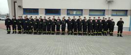 Grupowe zdjęcie uczestników szkolenia. Strażacy ustawieni w dwóch rzędach na tle jednego z budynków Szkoły