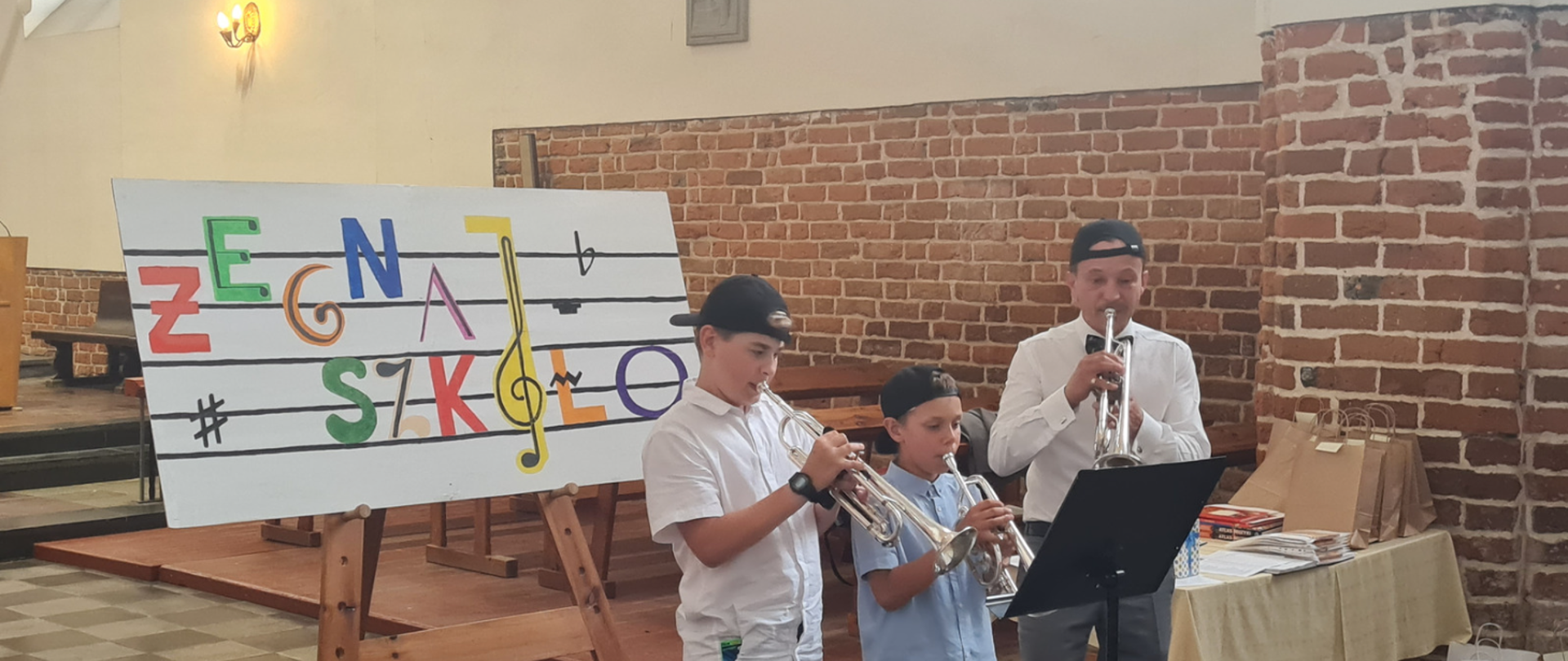 Zdjęcie z zakończenia roku szkolnego, które odbyło się w Kościele Szkolnym w Tczewie. Na zdjęciu baner z muzycznym napisem żegnaj szkoło oraz trębacze: Jerzy Kiedrowski, Konstanty Liss, p. Piotr Kowalkowski.