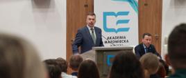 Widok od tyłu na salę, z przodu stoi za mównica minister Wieczorek i mówi do mikrofonu, za nim ścianka z napisem Akademia Mazowiecka.