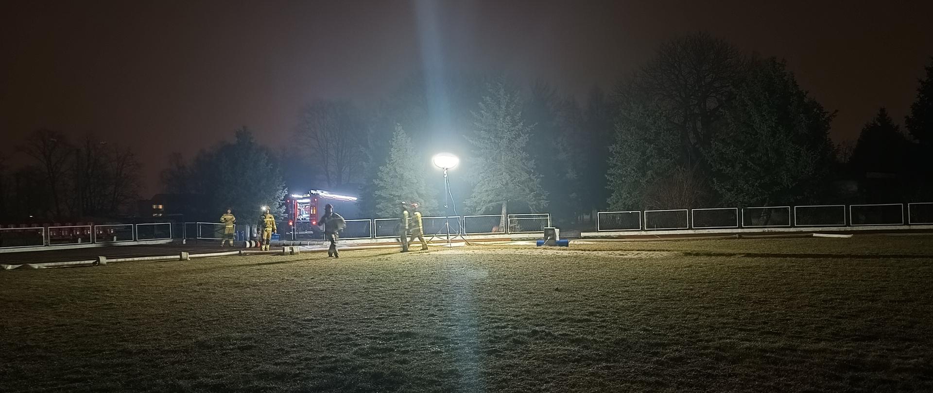 Nocne manewry z taktyki zwalczania pożarów z dostarczania wody na duże odległości dla słuchaczy szkolenia podstawowego w zawodzie strażak, ćwiczący strażacy na terenie boiska piłkarskiego