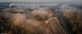 Zdjęcie lotnicze węzła na autostradzie A4. Zachodzące słońce, droga spowita mgłą przebiega przez las.