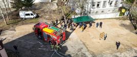 Widok na miejsce ćwiczeń. Widać wóz strażacki, namiot VIPów. Wszędzie dużo strażaków i żołnierzy. Zdjęcie wykonane z drona.