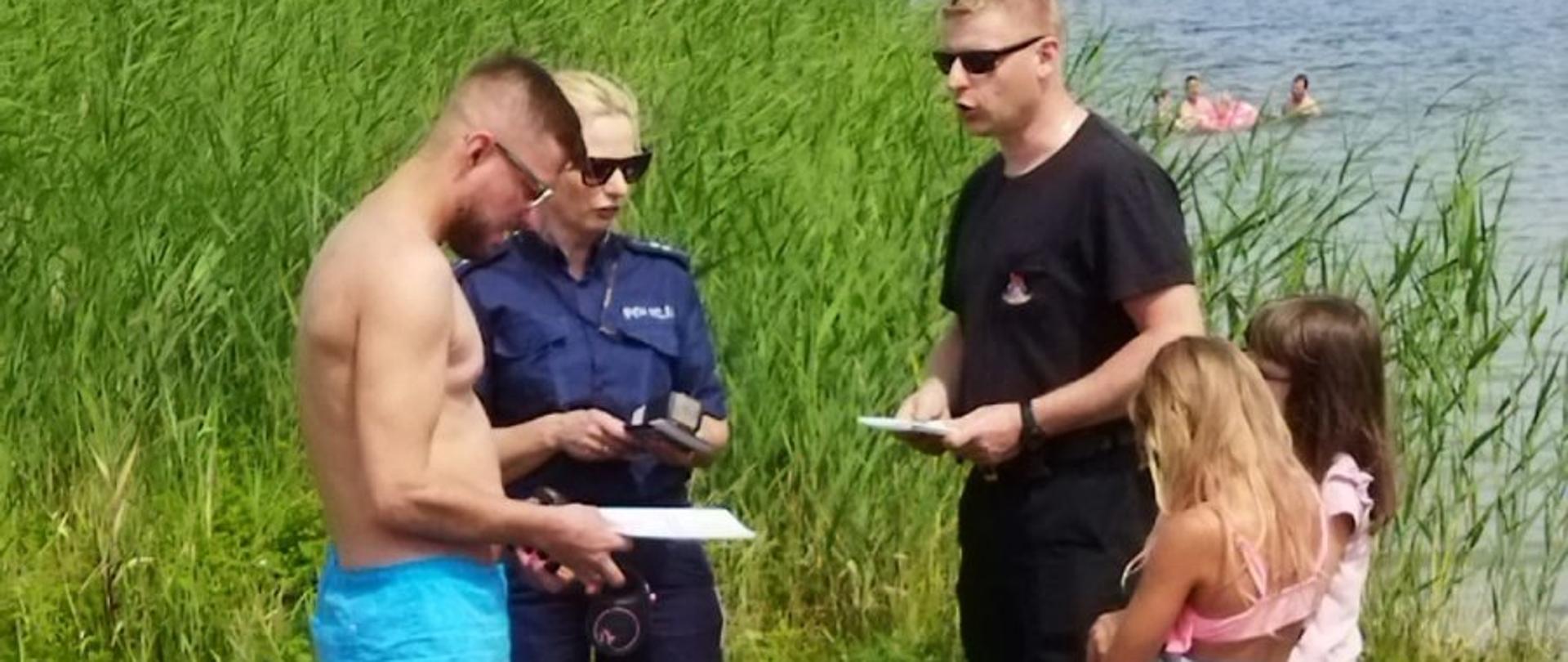 Strażak z policjantem omawiają zasady bezpiecznego przebywania nad woda.