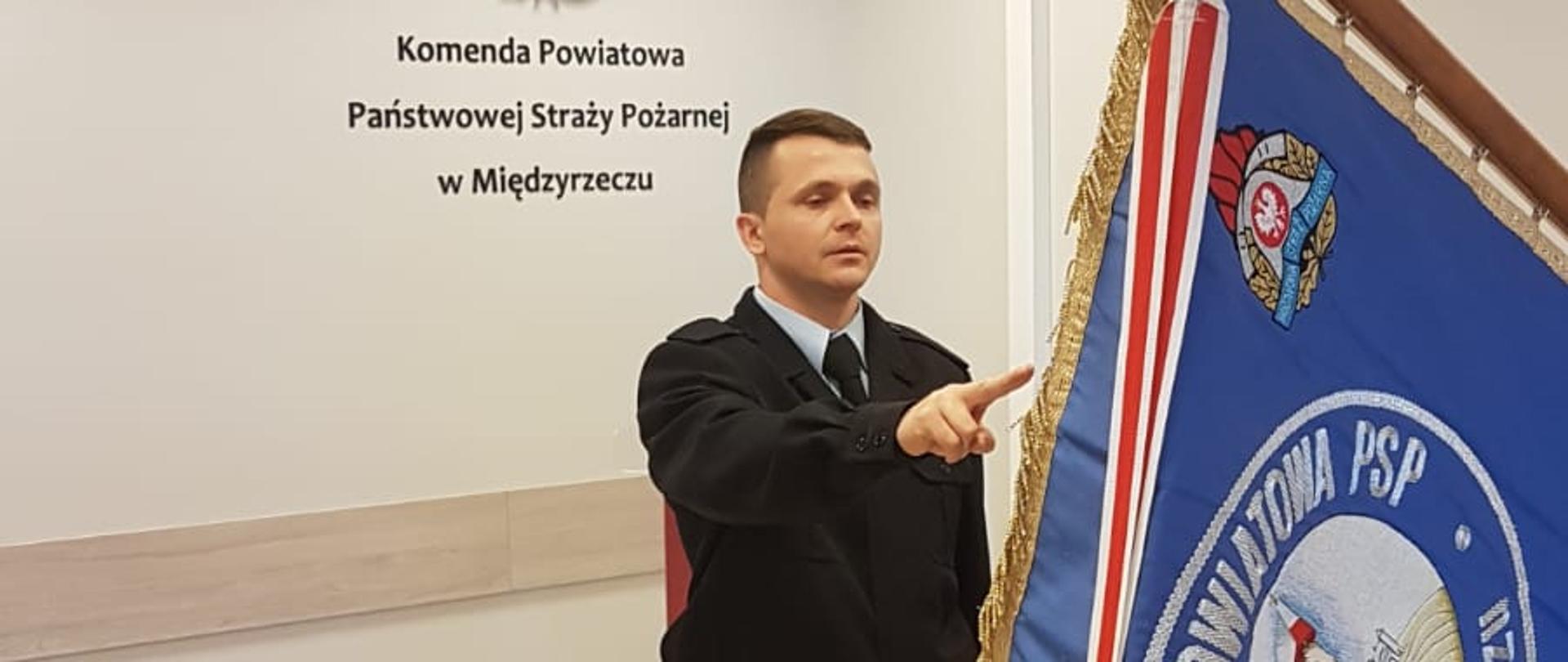 Zdjęcie przedstawia strażaka w mundurze służbowym składającego ślubowanie przed sztandarem KP PSP w Międzyrzeczu. 