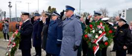 Przedstawiciele służb mundurowych składają kwiaty, oddając honory. 