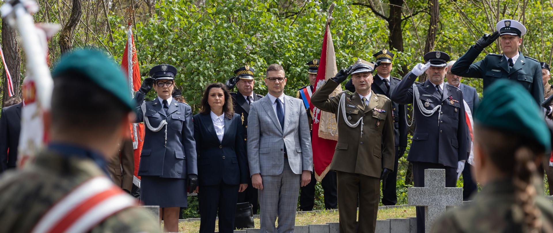 Wojewoda Kujawsko-Pomorski Michał Sztybel, Naczelnik Delegatury Instytutu Pamięci Narodowej w Bydgoszczy Edyta Cisewska podczas uroczystości na Cmentarzu Wojennym w Smukale. Towarzyszą im salutujący przedstawiciele służb mundurowych. Na pierwszym planie, odwróceni tyłem, żołnierze z kompanii honorowej. 
