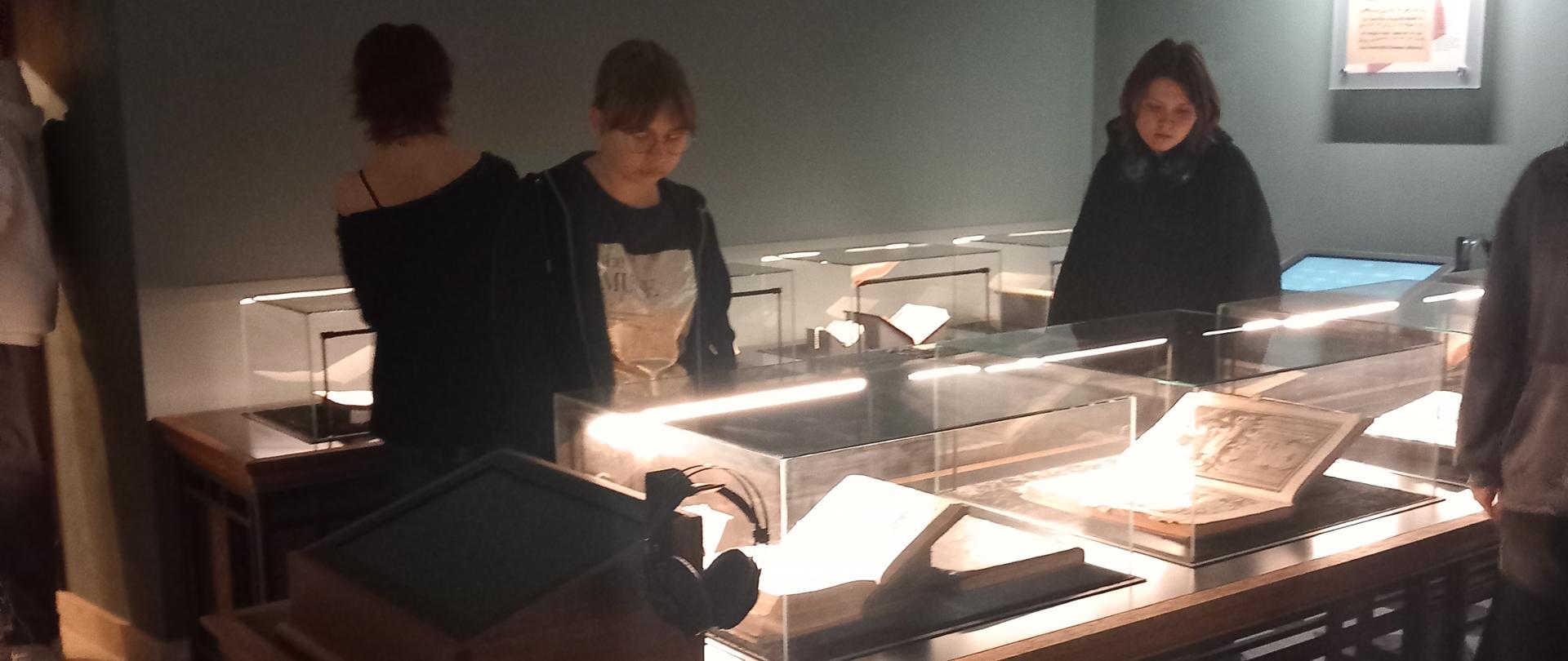 zdjęcie, sala muzealna, młodzież ogląda stare księgi w gablotach