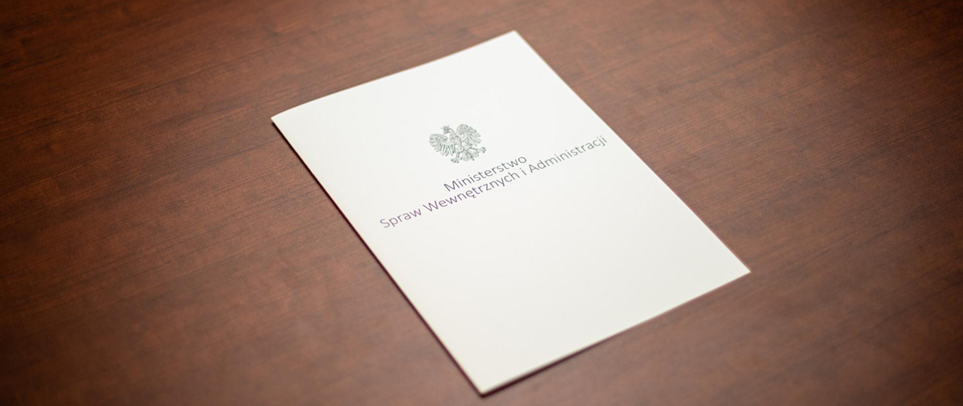 Na zdjęciu widać leżącą teczkę z napisem "Ministerstwo Spraw Wewnętrznych i Administracji" i orłem z godła narodowego.