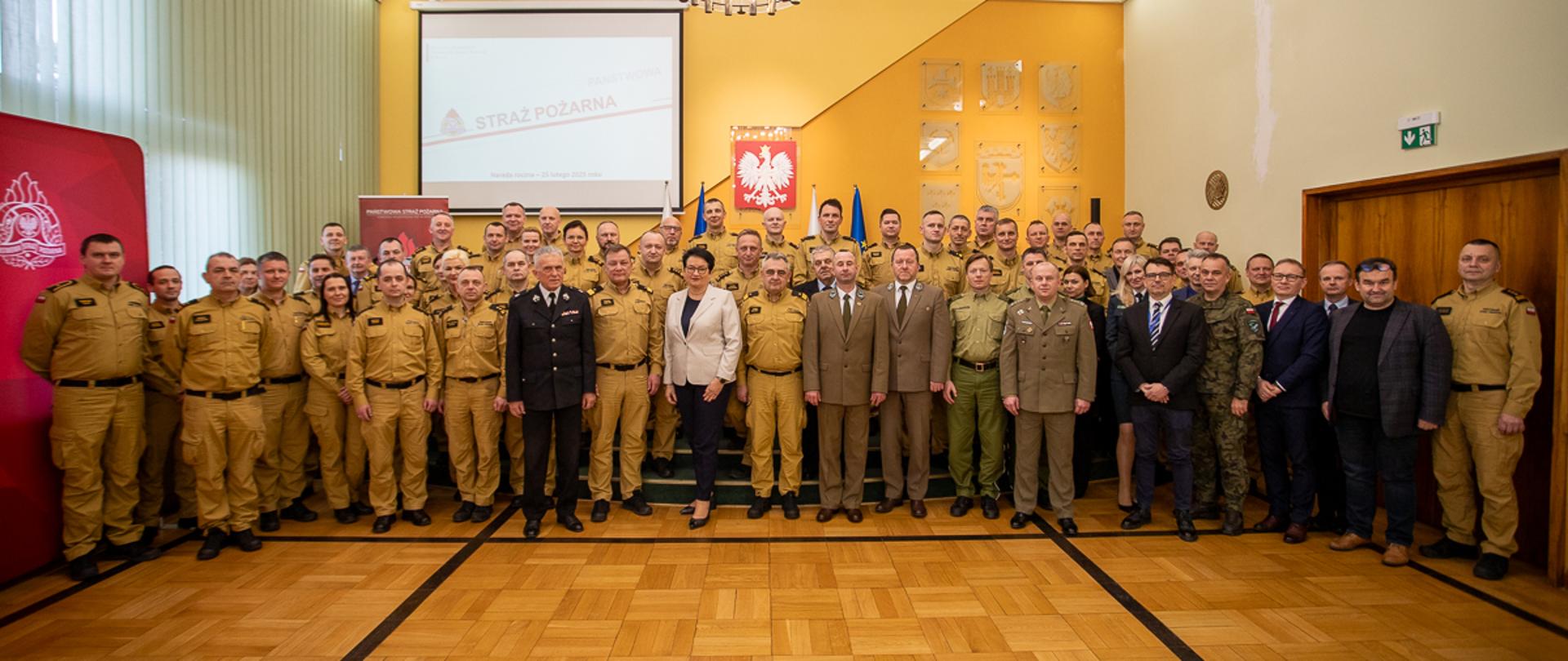 25 lutego 2025 roku w Sali Herbowej Opolskiego Urzędu Wojewódzkiego odbyła się narada kadry kierowniczej Państwowej Straży Pożarnej województwa opolskiego, podsumowująca działalność za rok 2024.
W spotkaniu uczestniczyli m.in. Wojewoda Opolski Monika Jurek, Zastępca Komendanta Głównego PSP nadbrygadier Józef Galica, Prezydent Opola Arkadiusz Wiśniewski, Prezes Zarządu Wojewódzkiego ZOSP RP w Opolu dh Andrzej Borowski oraz przedstawiciele innych służb i instytucji. W naradzie ponadto uczestniczyli kierownicy wydziałów KW PSP w Opolu oraz komendanci i zastępcy komendantów powiatowych i miejskiego PSP z terenu Opolszczyzny.
Wspólne zdjęcie grupowe uczestników narady. Strażacy PSP w umundurowaniu służbowym. Druh OSP oraz inne służby w umundurowaniu wyjściowym.