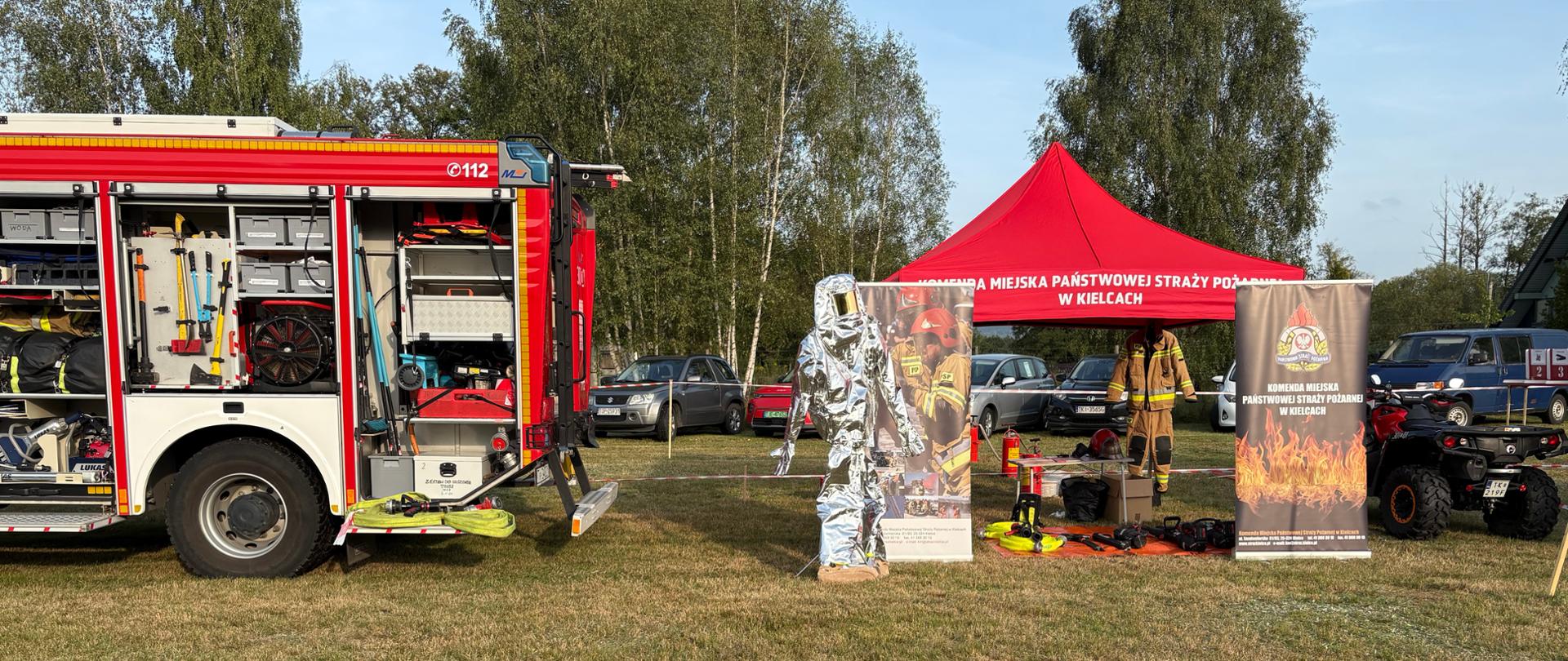 Zdjęcie przedstawia stoisko edukacyjne Komendy Miejskiej Państwowej Straży Pożarnej w Kielcach, z lewej strony udostępniony dla zwiedzających samochód gaśniczy, a z lewej strażacki quad.