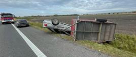 Zdjęcie przedstawia pojazd Audi w pozycji na dachu oraz przyczepkę samochodową w pozycji na boku leżące na poboczu DK nr 78. W tle widać pojazdy pożarnicze