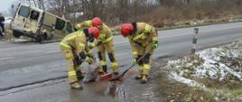 Kolizja dostawczaków. Droga gminna w Dębnie Polskim. Na pierwszym planie trzech strażaków usuwających zanieczyszczenia z jezdni. Jeden z nich trzyma plastikowy worek, pozostali - miotłę i szuflę. W tle, jedno z aut uczestniczących w kolizji, przodem w rowie.
