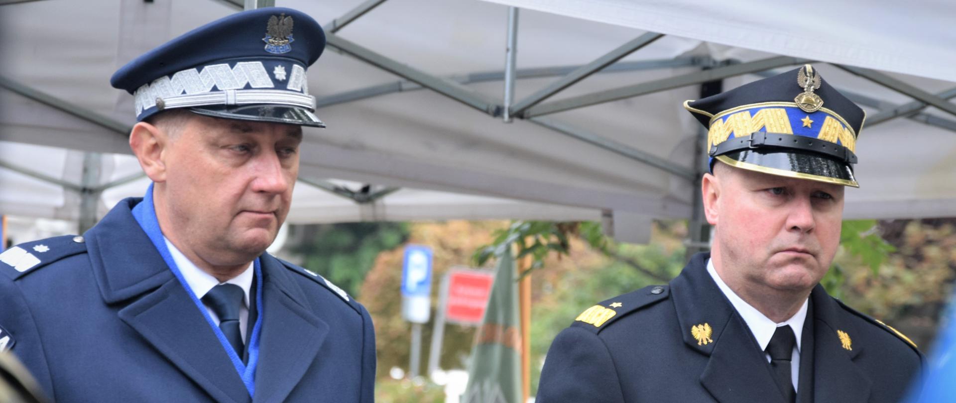 dwóch mężczyzn w mundurach stoi na baczność, mężczyzna z lewej strony to policjant, mężczyzna z prawej to strażak